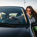 Young frustrated Caucasian woman pushing car along road alone.